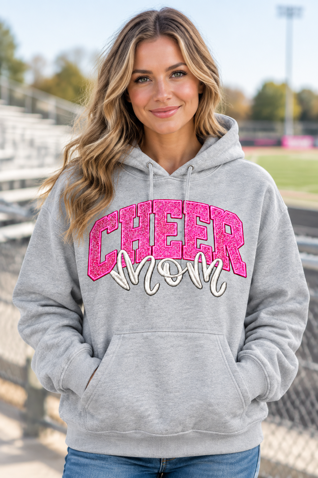 AI-generated model mockup of a woman wearing the gray Cheer Mom Glitter Hoodie with pink CHEER lettering and white mom script.